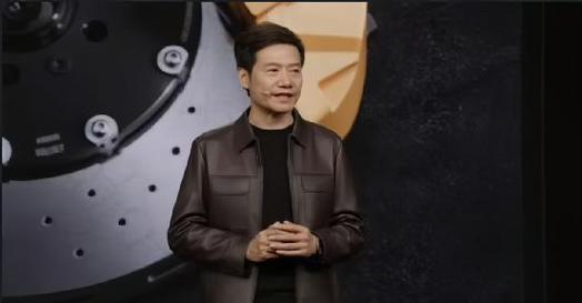 （聚光灯亮起，雷军身着标志性黑色高领衫走上舞台，手持激光笔在投影幕布上划出一道金色弧线）